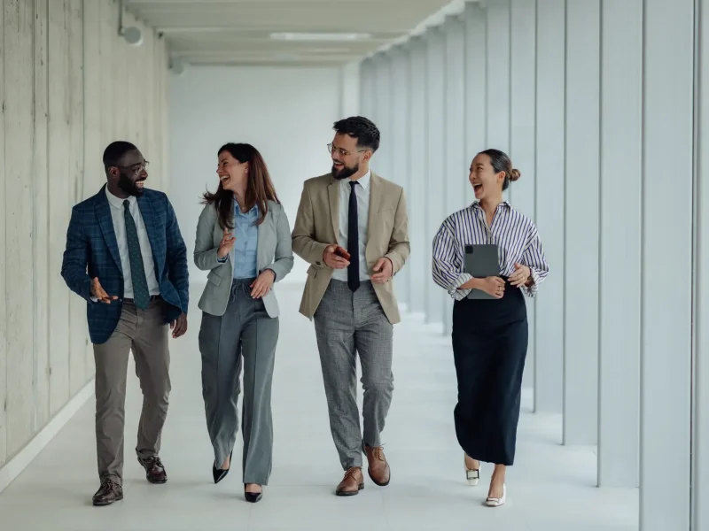 Happy multiethnic businesspeople walking and talking in office hallway